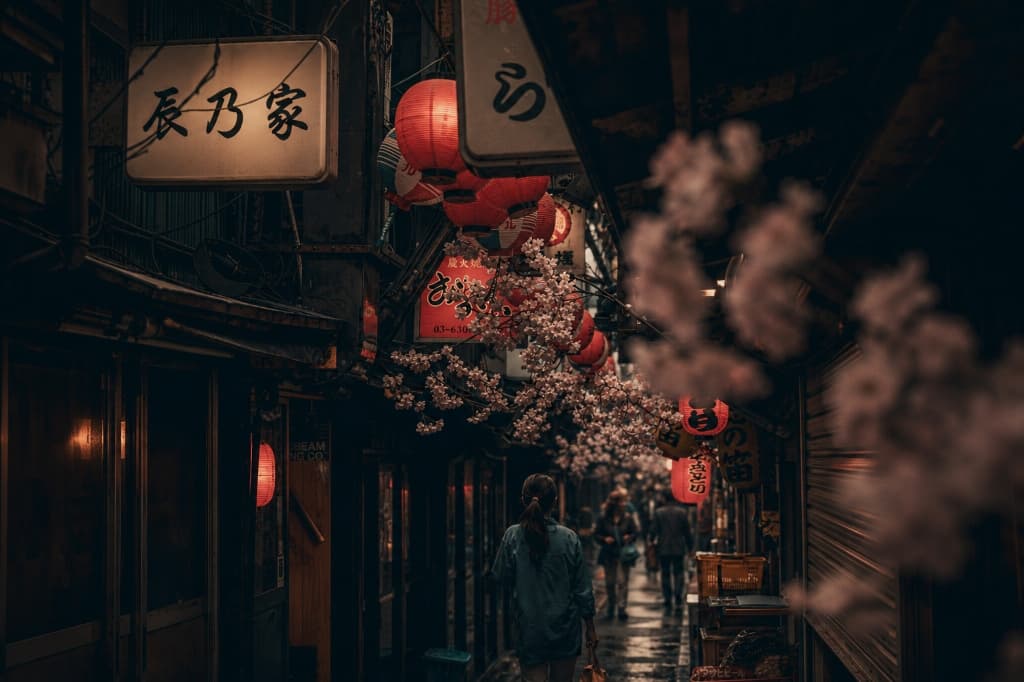 Atmospheric Tokyo alleyway in Shinjuku framed with cherry blossoms, glowing red lanterns, and traditional shop signs